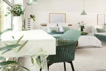 Interior of stylish hotel room with houseplants, table and cozy bed