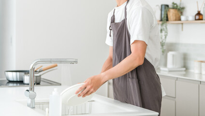 Young Asian man in an apron washing dishes in the kitchen
