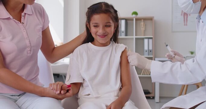 Doctor gives an injection to a child as a mother holds her hand, supporting vaccination and immunization in a healthcare setting for protection and smile. Child gets vaccine shot in medical clinic.