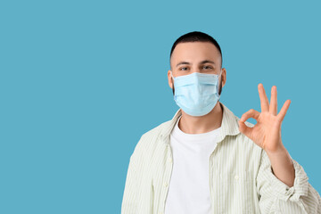 Young man in medical mask showing OK gesture on blue background