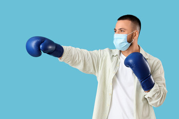 Young man in medical mask and boxing gloves on blue background