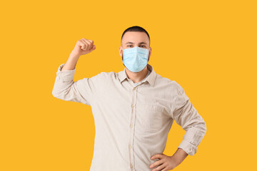 Young man in medical mask showing muscles on yellow background