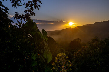 Sunset over the mountains with lush greenery under the golden sky in a serene landscape