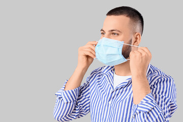 Happy young man wearing medical mask on grey background