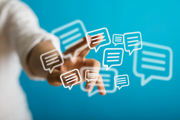 A hand interacting with digitally rendered speech bubbles, representing online communication, social media, and virtual connection on blue backg