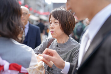 A woman in a gray shirt is talking to a man in a suit. The man is holding a handbag