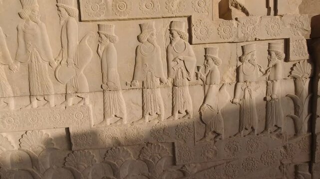 Tracking along an Achaemenid stone relief at Persepolis, Iran: bearded courtiers in procession beneath carved rosettes, crisp sunlight and ancient textures evoking empire, ritual, timeless heritage.