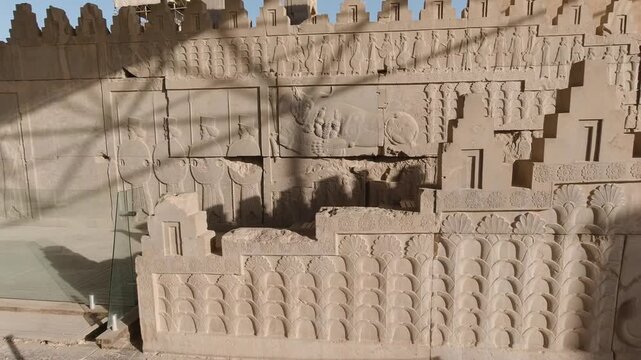 Smooth tracking along Persepolis stone reliefs at golden hour, featuring the iconic lion and bull motif with adjacent guard panels&mdash;carved textures and shadows highlighting Achaemenid artistry.