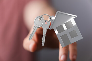 Hand holding house keys in front of a house cutout. Perfect for real estate, home buying, and...