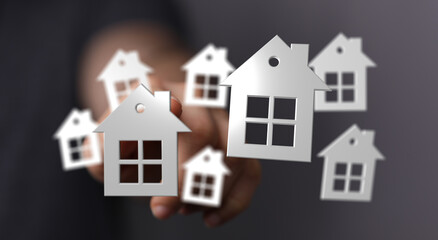 An abstract conceptual image of a person's hand holding several white paper house cutouts, representing real estate or home ownership.