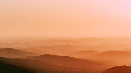 Obraz premium Layered mountain ridges fade into the warm hazy glow of sunset or sunrise