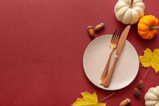 Beautiful table setting with autumn leaves, acorns, pumpkins and pine cones on red background - Powered by Adobe