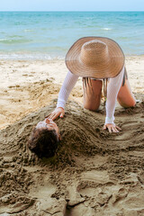 Colombian aunt shaping sand over buried nephew at Caribbean beach, playful moment in Coveñas.