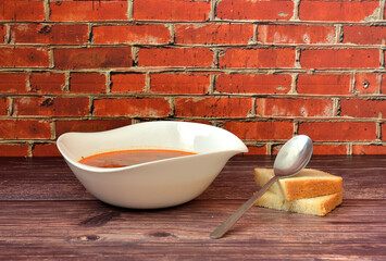 A plate of tasty rich soup and two pieces of wheat bread with a spoon on a wooden table.