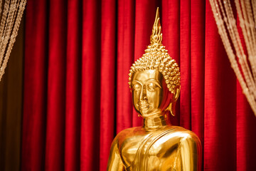 Fototapeta premium Brightness golden Buddha is sitting meditation in front of red scarlet curtain.