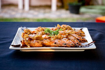 Crispy prawns in tamarind sauce in  white square dish, sprinkle with glaze and top with fried shallots and coriander. It has perfect balance of crispy, spicy, and sweet flavors.