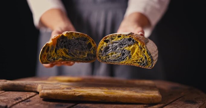 Woman baker shows how soft and elastic is rustic artisan homemade crusty sourdough bread oven baked with activated carbon, curcuma spice and pumpkin video
