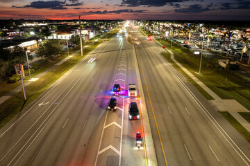 Nighttime traffic stop on USA city street as police pull over speeding vehicle. Patrol car lights flash in urban traffic environment. © bilanol