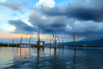 Obraz premium Serene Rawa Pening Lake With Wooden Poles and Small Fishing Hut Called Branjang At Sunset Under Dramatic Clouds