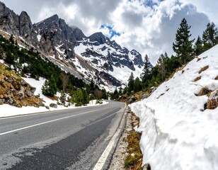 A road cuts through a mountain pass, flanked by snow, rocks, and sparse trees under cloudscape