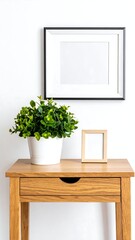 Wooden table with plants and frames against white wall
