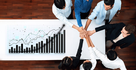 A collaborative meeting showing diverse professionals joining hands over a table with financial graphs, representing teamwork and business growth strategies. Axiom