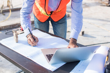 Construction worker wearing a working suit with helmet, holding a pen and looking at the papers...