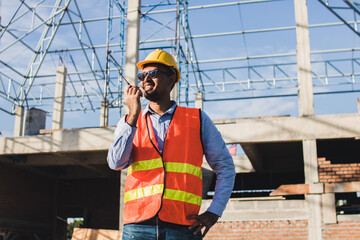 Male Construction worker or Engineer or Foreman stands at a building site  using a walkie-talkie radio to coordinate and consulting with the team