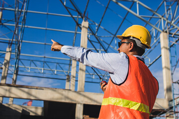 Male Construction worker or Engineer or Foreman stands at a building site  using a walkie-talkie radio to coordinate and consulting with the team