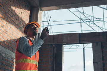 Male Construction worker or Engineer or Foreman stands at a building site  using a walkie-talkie radio to coordinate and consulting with the team