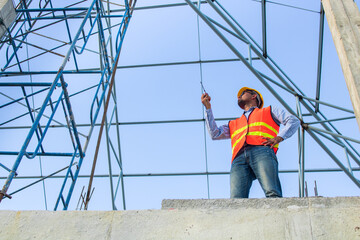 Male Construction worker or Engineer or Foreman stands at a building site  using a walkie-talkie radio to coordinate and consulting with the team