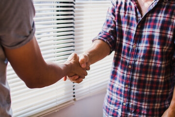 Two construction professionals shaking hands over blueprints and safety equipment signifying a successful project agreement and partnership