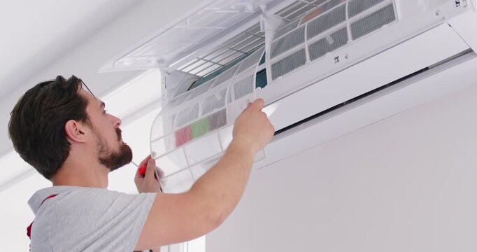 Repairman from the AC maintenance service takes care of the air conditioner in the house. Young male worker changes filters in a modern air conditioner on the wall at home