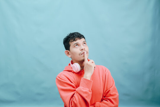 Young man in orange hoodie thinking deeply on blue background. - Powered by Adobe