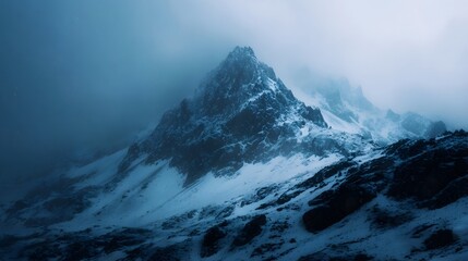 A dramatic snow covered mountain peak emerges from the fog under a twilight sky