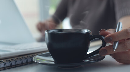 Close up, business woman hand holding a cup of coffee during online working on laptop computer at home office, freelance at work, taking a coffee break, people lifestyles