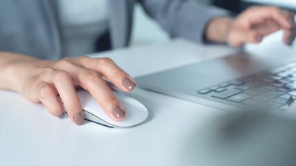 Business woman hand holding and clicking wireless computer mouse, working on laptop, surfing the...
