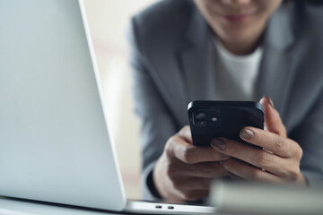 Businesswoman using smartphone in office during working on laptop computer, typing, touching the screen, browsing the internet or online messaging, social media network
