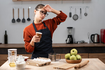 sick sad housewife baker woman put hand on forehead have headache drinking takeaway coffee working...