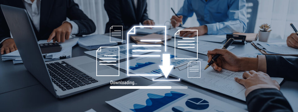 Professionals engage in a business meeting, discussing document downloads and strategic planning with charts and laptops, showcasing teamwork and productivity in an office setting. Trope - Powered by Adobe