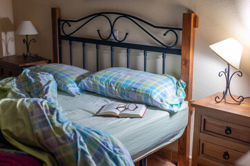 Cozy Bedroom Bed With Open Book and Glasses on Nightstand and Bedside Lamps
