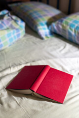 Red Notebook Resting on a Soft Bed With Colorful Plaid Pillows in a Cozy Bedroom