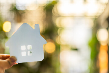 Hand holding white house symbol with soft bokeh background represents dream home, real estate...