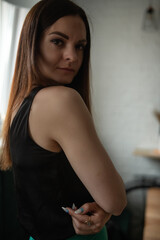 Young woman with long dark hair, wearing a black top, gazes thoughtfully out of a window, illuminated by natural light, creating a serene and contemplative atmosphere