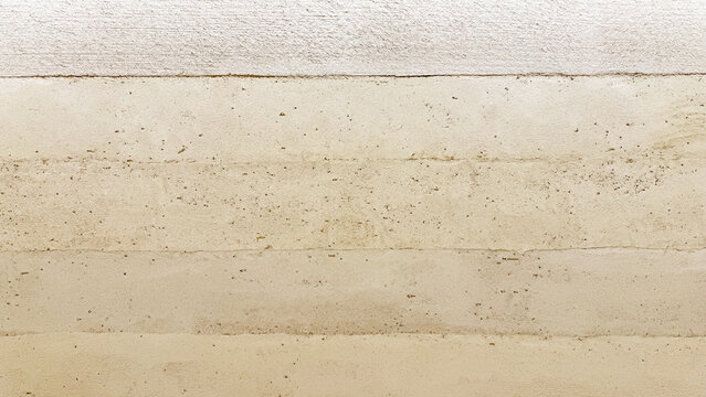Close-up of a modern, eco-friendly rammed earth wall showcasing horizontal layers, natural warm tan and beige tones, and a subtly textured, sustainable building surface.