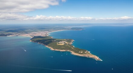 Aerial view of coastal town and verdant peninsula jutting into blue ocean