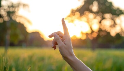 A hand pointing upwards against a warm, blurred golden sunset