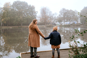 Mother and daughter holding hands by a foggy lake.