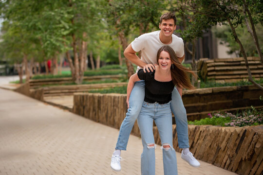 Laughing couple in park as woman gives man a piggyback ride - Powered by Adobe
