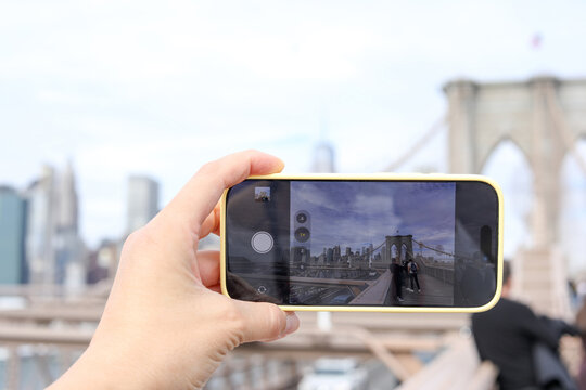 Woman holding cellphone taking snapshot on Brooklyn Bridge